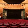 An empty auditorium with rows of red seats facing a stage, ready for an event.