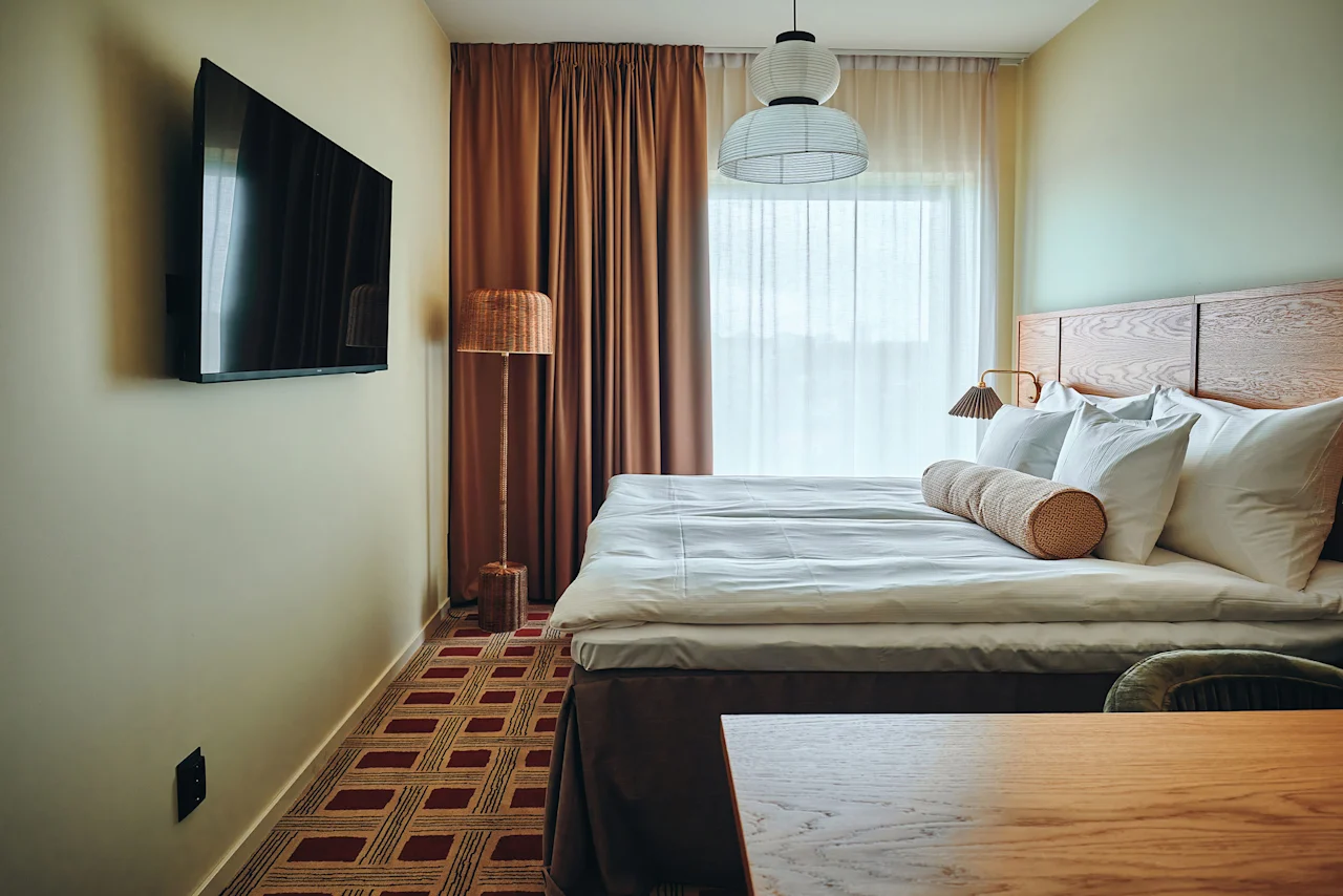 Et koselig hotellrom med en stor seng, en veggmontert TV og varm belysning, klart for et komfortabelt opphold.