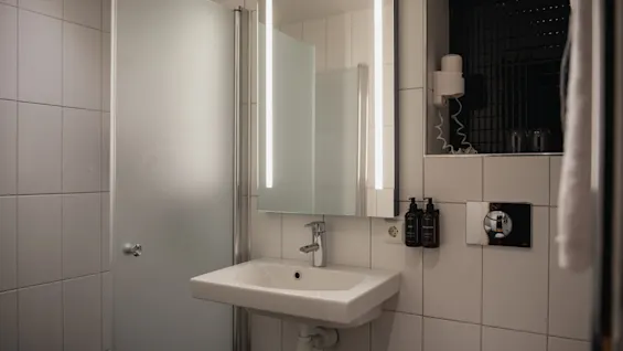 Ett rent och modernt hotellbadrum på Home Hotel Grand, Helsingborg, med handfat, belyst spegel och dusch.