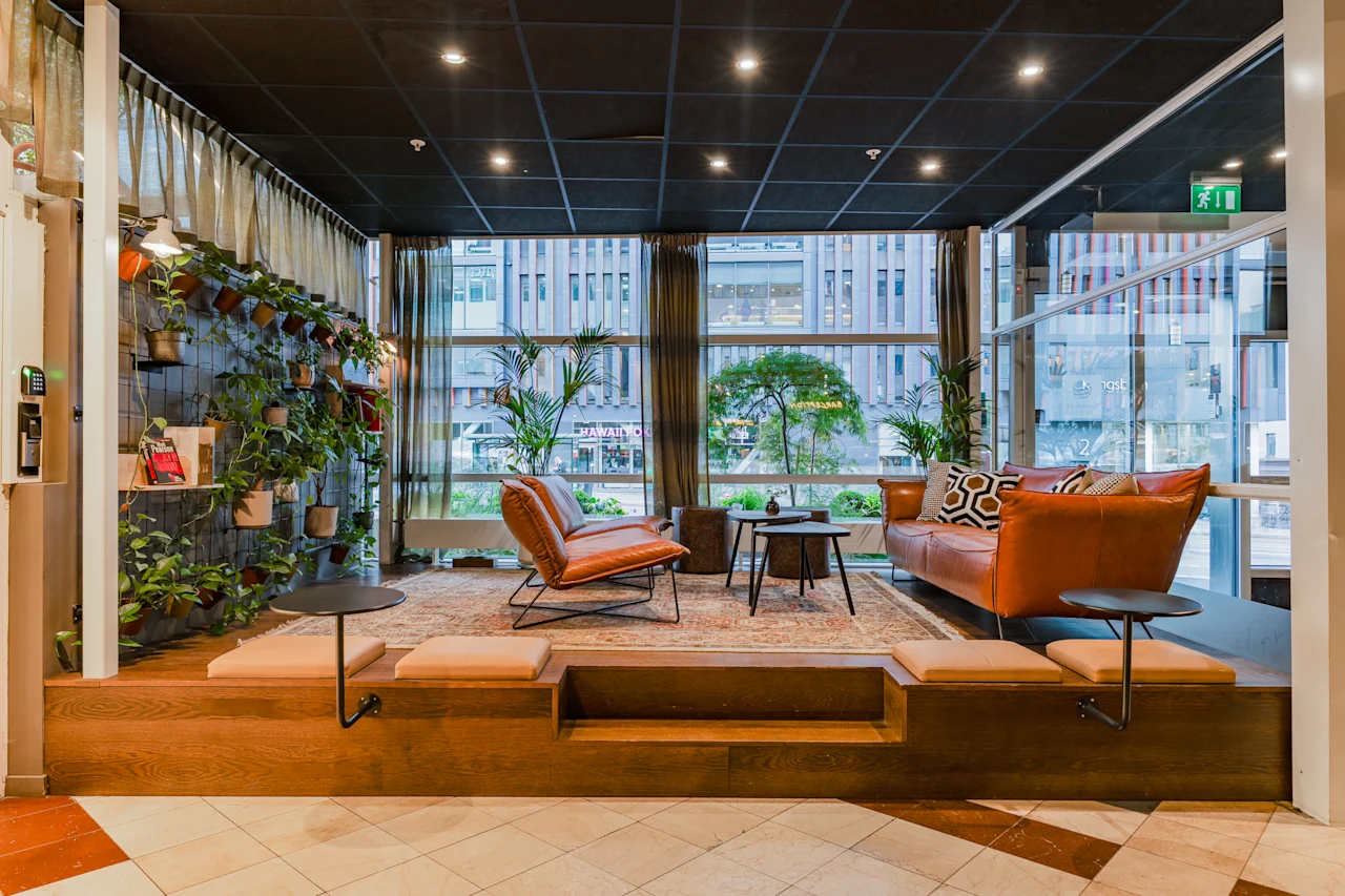 A modern and cozy hotel lobby lounge with leather seating, green plants, and large windows.