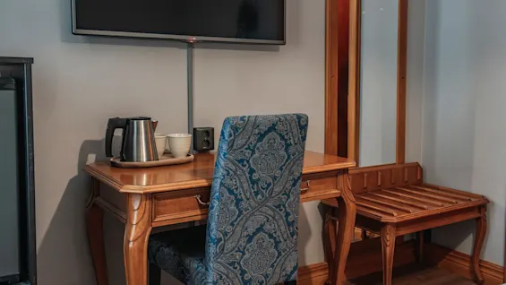 En mysig hotellrumshörna med ett träskrivbord, en mönstrad stol, en vattenkokare för varma drycker och en TV för underhållning.