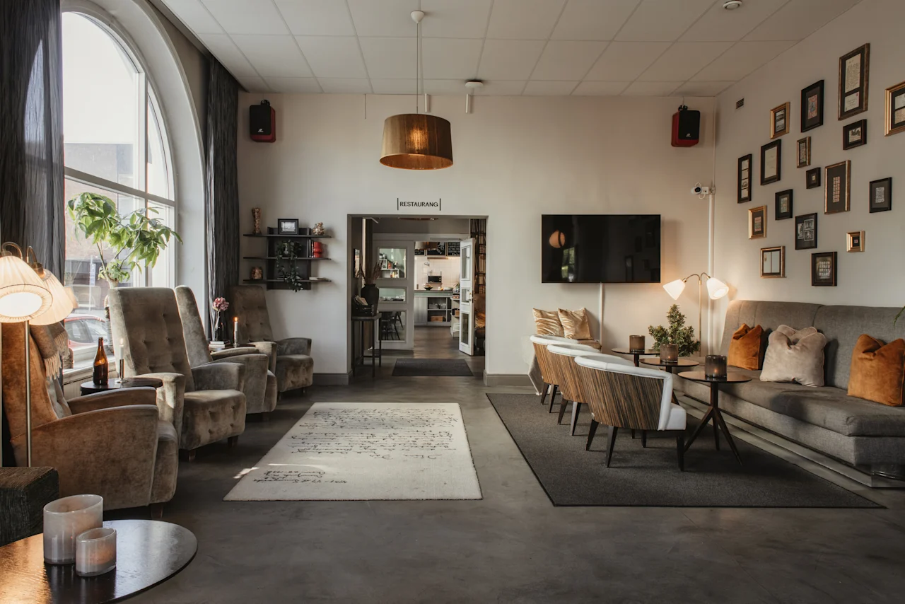 Ett bekvämt hotelloungeområde med olika sittplatser, ett stort välvt fönster och en ingång till RESTAURANG.