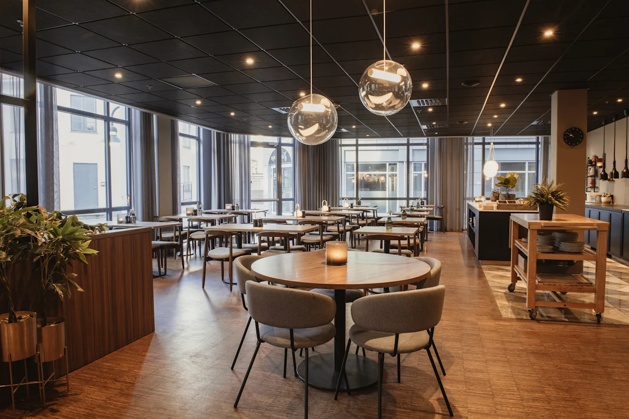 En moderne, tom hotellrestaurant med mange bord og stoler, store vinduer og serveringsstasjoner, klar for gjester.