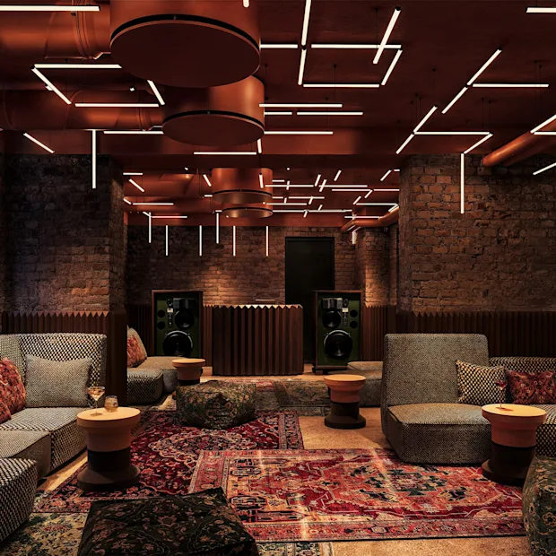 A cozy, modern lounge with brick walls, comfortable sofas, oriental rugs, and unique geometric ceiling lights.
