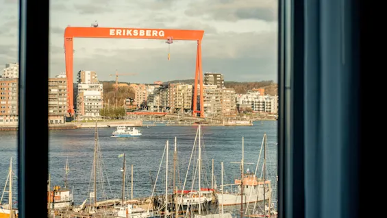 Näkymä ikkunasta satamaan, jossa on veneitä, rakennuksia ja suuri oranssi nosturi, jossa lukee ERIKSBERG.