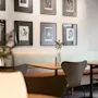 Ett matutrymme med moderna stolar och bord med små växter, inramad konst på ljusa väggar och mjuk hängande belysning, vilket skapar en mysig, modern atmosfär.
