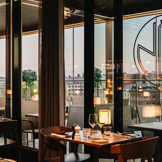 En mysig restaurang på Clarion Hotel Sundsvall med dukade bord, stadsvy genom stora fönster och utomhusterrass.