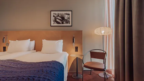 Viihtyisä hotellihuone, jossa on sijattu sänky, tyylikäs tuoli ja lämmin valaistus.