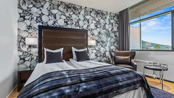 Ett mysigt hotellrum med en stor säng, en bekväm fåtölj och ett fönster med naturskön utsikt över bergen.