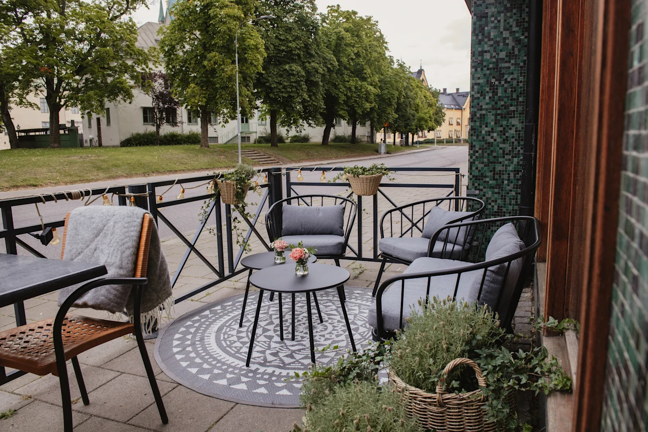 An inviting outdoor patio with comfortable seating and small tables, adorned with plants, next to a quiet street.