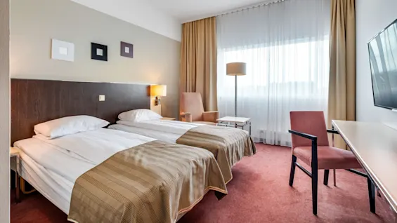 A tidy hotel room with two twin beds, a chair, desk, lamp, and flat-screen TV.