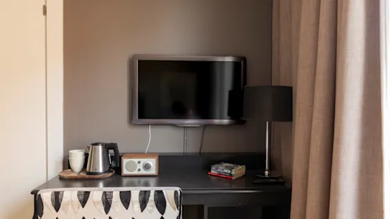 En mysig skrivbordsplats i ett hotellrum med TV, vattenkokare, radio och lampa, redo för arbete eller avkoppling.