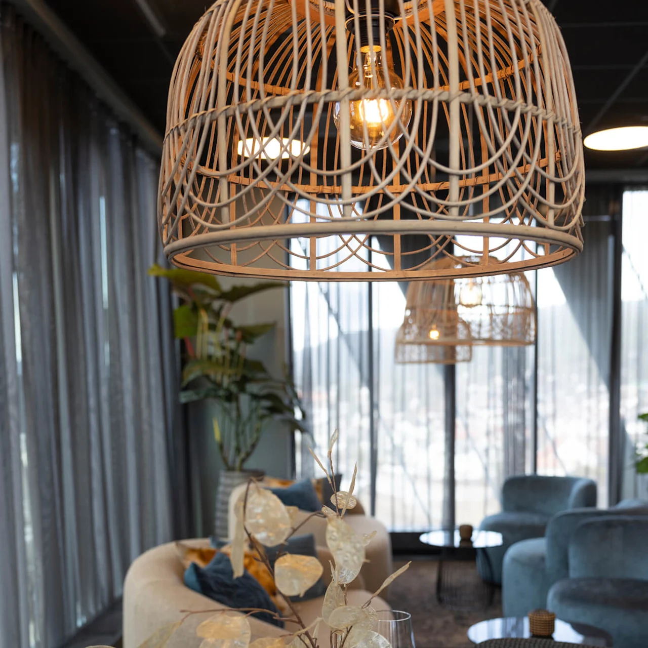 A dining area with elegant table settings, oversized wicker pendant lights overhead, and stylish sofas in the background.
