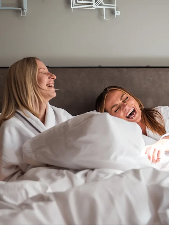 Two people in bathrobes laughing joyfully in bed.