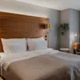 Et koselig hotellrom med en stor seng, sengegavl i tre og varm belysning, med en komfortabel lenestol og et snev av grønt.