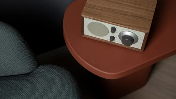 A vintage-style radio with a wooden case and silver face sits on a reddish-brown table next to a grey chair, suggesting a cozy listening experience.
