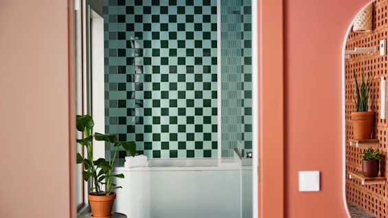 A modern bathroom with green checkered tiles, a white bathtub, and potted green plants.