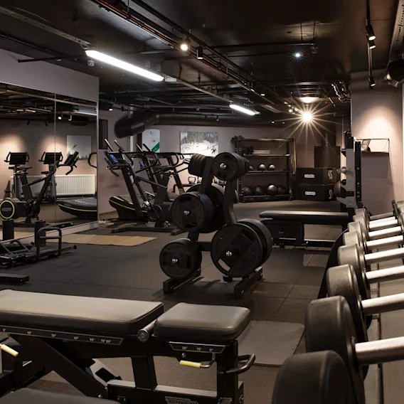Modernt hotellgym utrustat med hantelställ, viktskivor, träningsbänkar, speglar och träningsmaskiner.