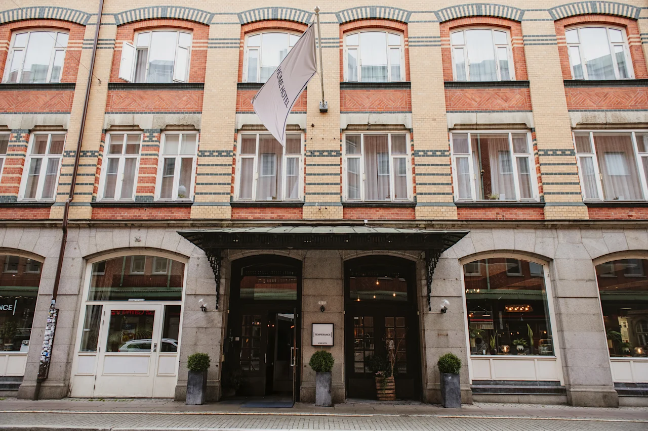 En fleretagers bygning med murstens- og stenfacade, med en fremtrædende indgang med markise og et flag, der viser HOME HOTEL.