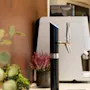 A modern beverage dispenser with a sleek tap, surrounded by decorative plants, in a cozy break area.