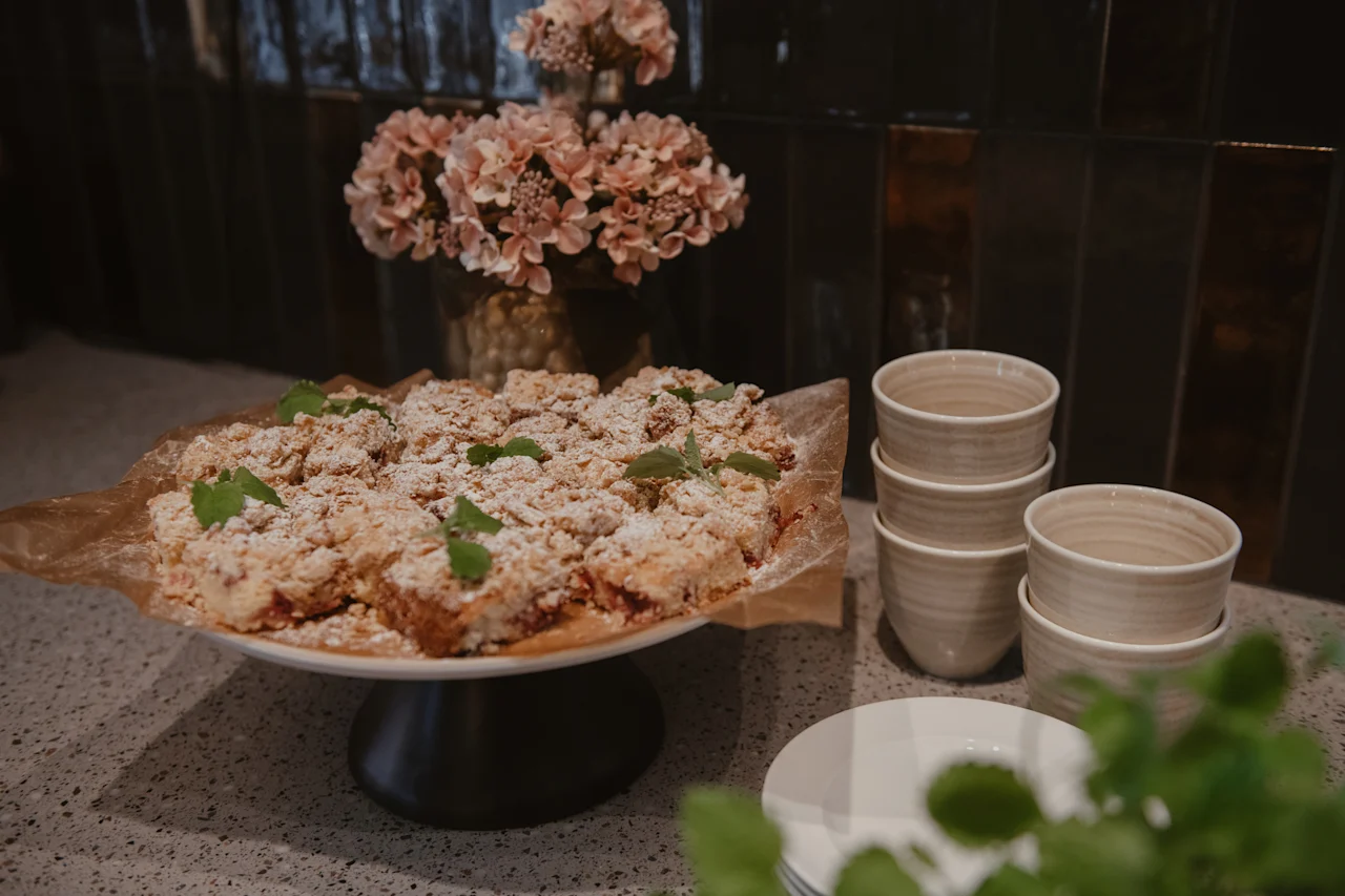 Et deilig dessertbord med smuldrepai-biter drysset med melis og mynte, sammen med stabler av keramiske kopper og tallerkener, klare til servering.