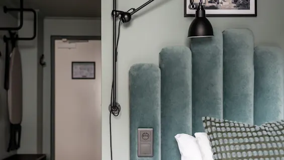 Et moderne hotellrom med en myk turkis sengegavl, en fleksibel leselampe og en tilgjengelig stikkontakt for gjester.