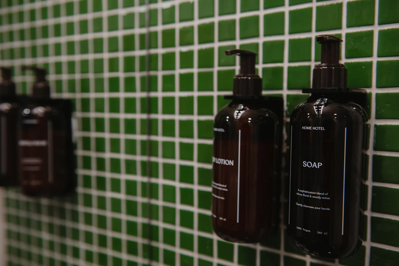 Two dark bottles of LOTION and SOAP mounted on a green tiled wall at Home Hotel Uppsala.