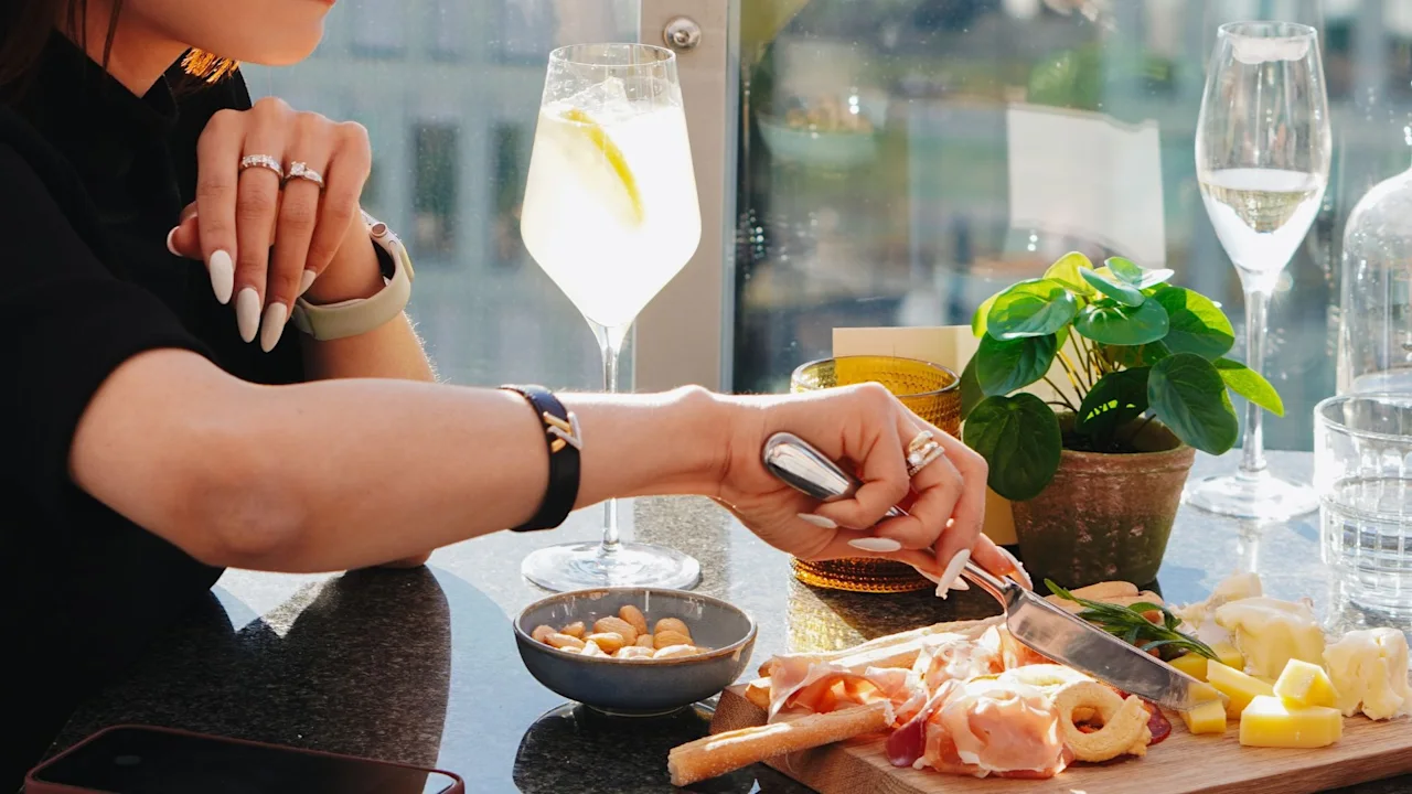 A person enjoying an outdoor meal with charcuterie, cheese, and a refreshing drink, overlooking a scenic view.