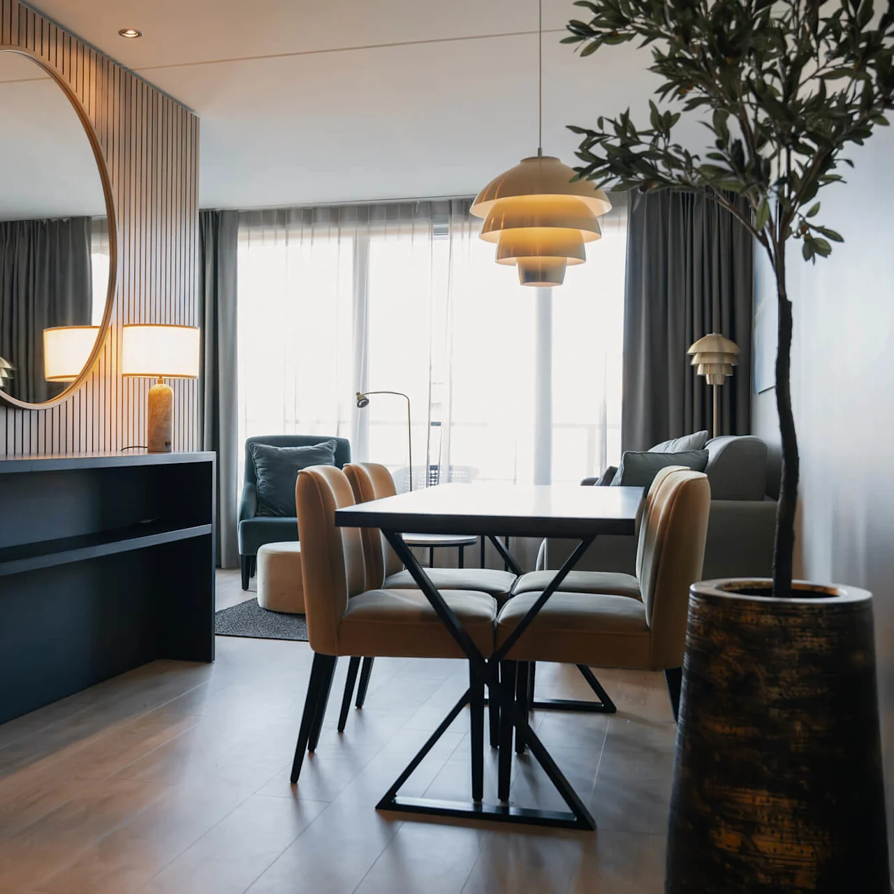 Spisebord med stoler står i en moderne stue. Et stort rundt speil er montert på en trevegg og reflekterer en lampe ved siden av en mørk konsoll.
