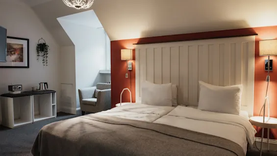 Ett välkomnande hotellrum på Home Hotel Grand, Helsingborg, med en säng med vit sänggavel, varm belysning och en liten sittgrupp.