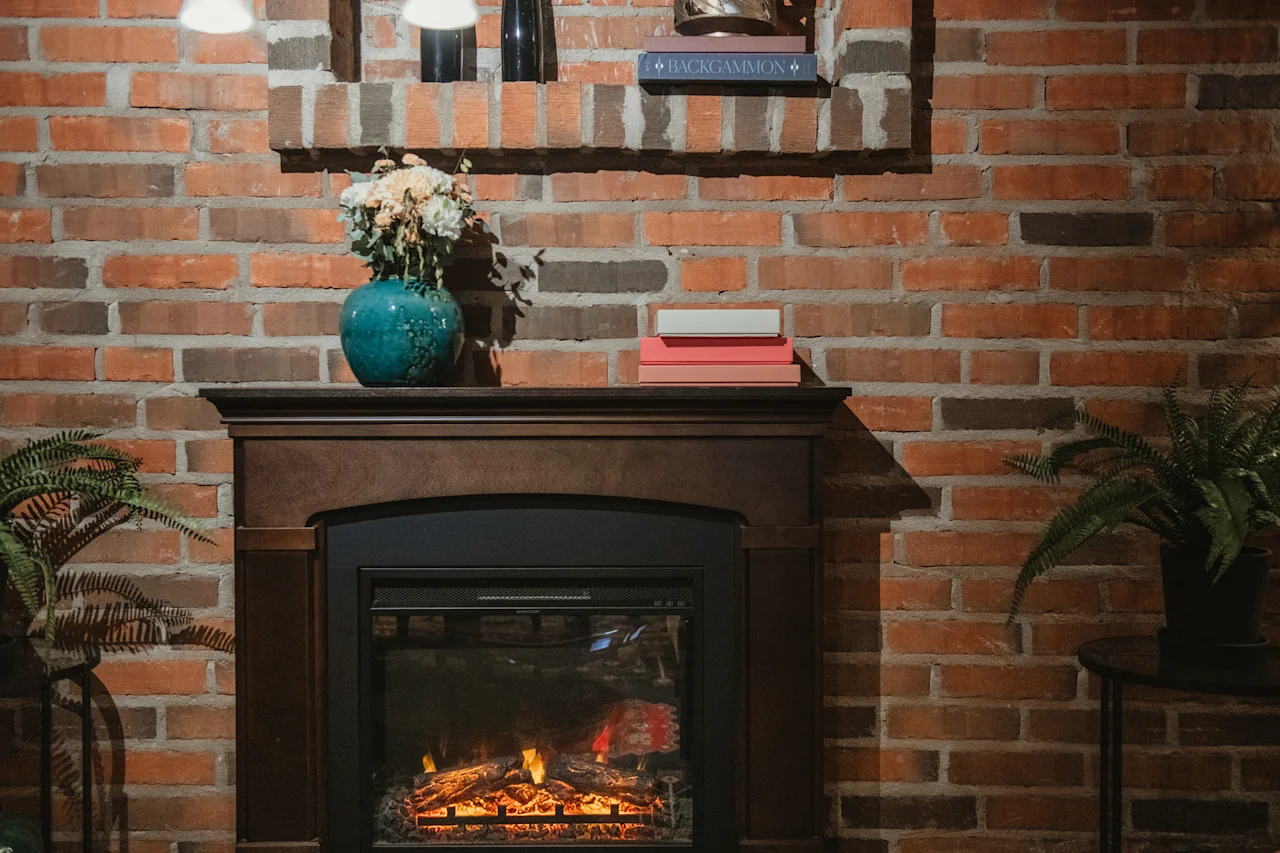 En mysig öppen spis med en tegelvägg, prydd med en vas med blommor och böcker, inklusive en med titeln BACKGAMMON. En varm eld glöder inuti.