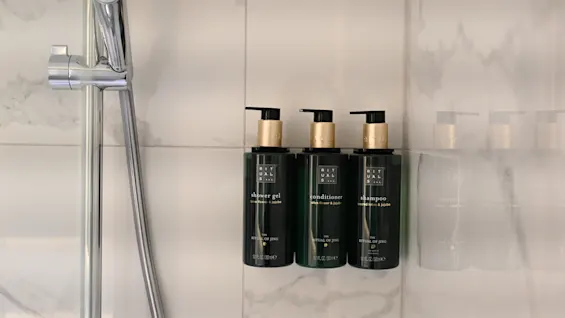 Et dusjområde med tre mørkegrønne flasker med dusjsåpe, balsam og sjampo montert på en flislagt vegg.