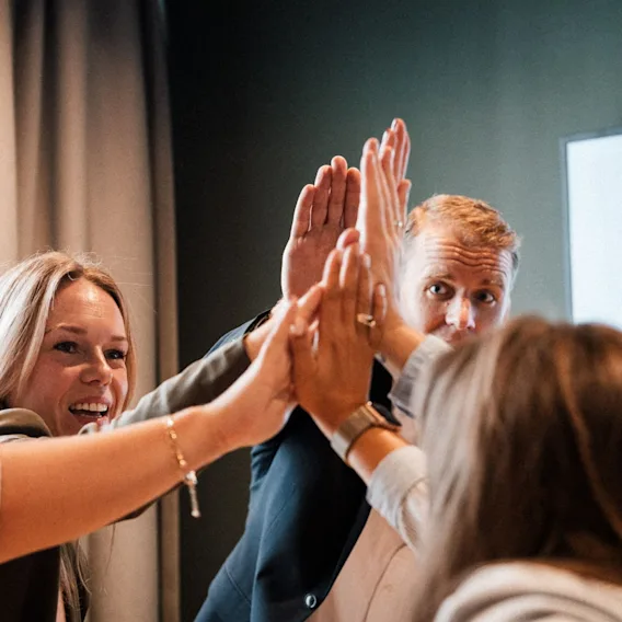 En gruppe smilende kollegaer som feirer godt samarbeid med en high-five under et møte.