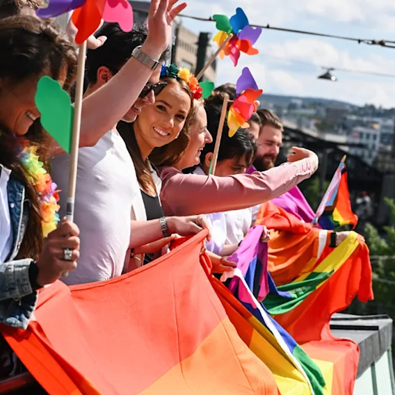 En gruppe mennesker som står på en balkong og vifter med Pride-flagg