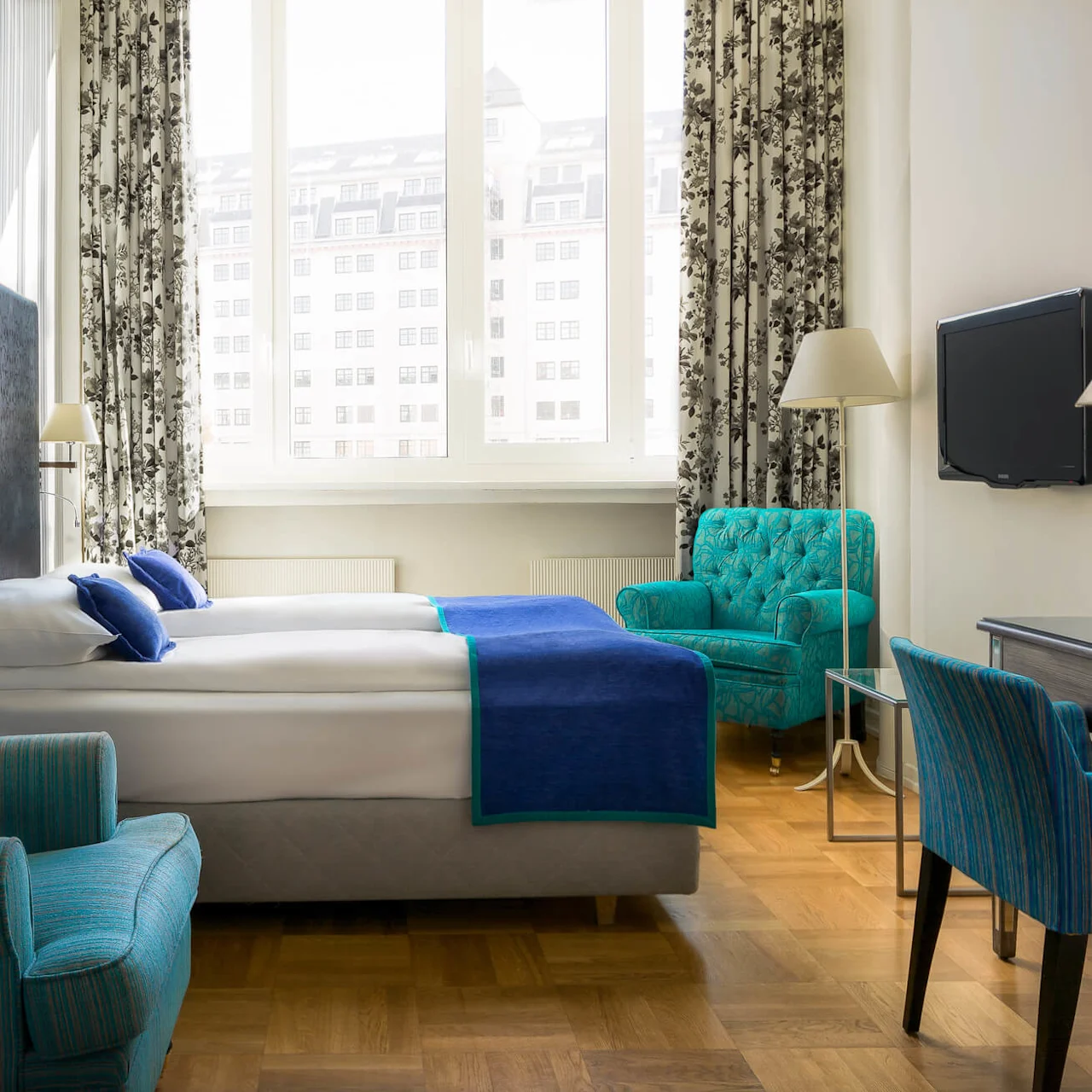 Et pent arrangert hotellrom med en stor seng, lenestoler, og en TV, som viser en koselig og moderne atmosfære.