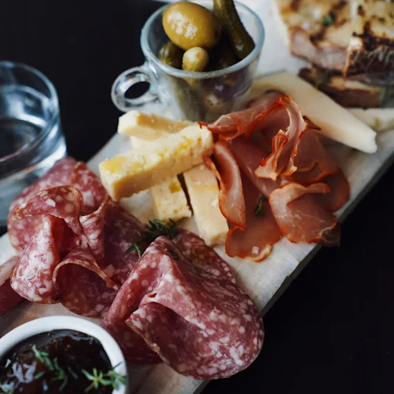 Et deilig spekefat med salami, skinke, ost, sylteagurk og oliven servert på en trefjøl.
