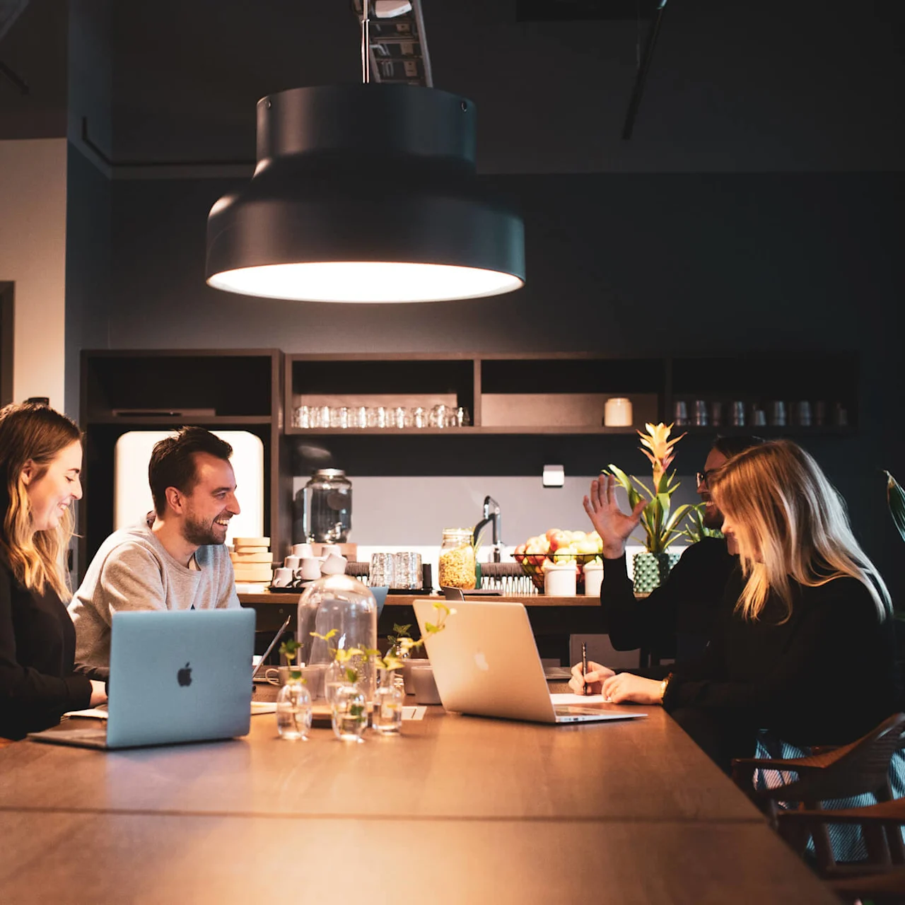 Three people are working at laptops in a modern kitchen with subdued lighting.