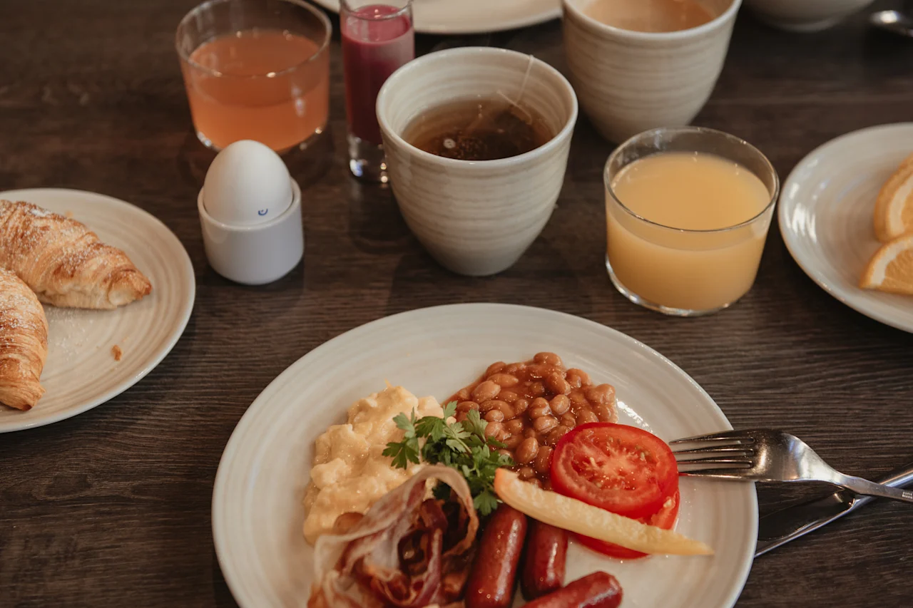 En lockande frukostbuffé på ett träbord, med en tallrik varm mat, färska croissanter, fruktjuicer och te.