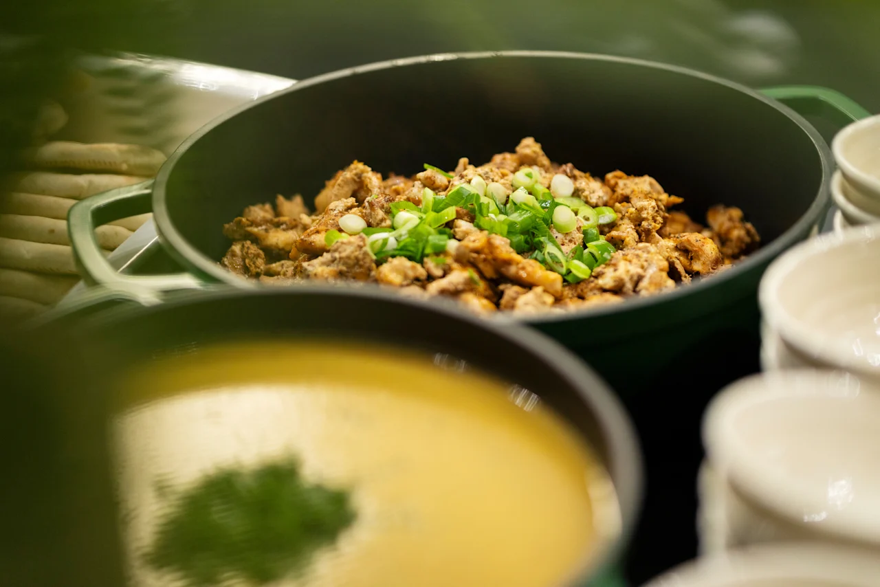 A buffet spread featuring a pot of seasoned chicken with green onions and a pot of creamy soup. Home Hotel Grand Bodø.