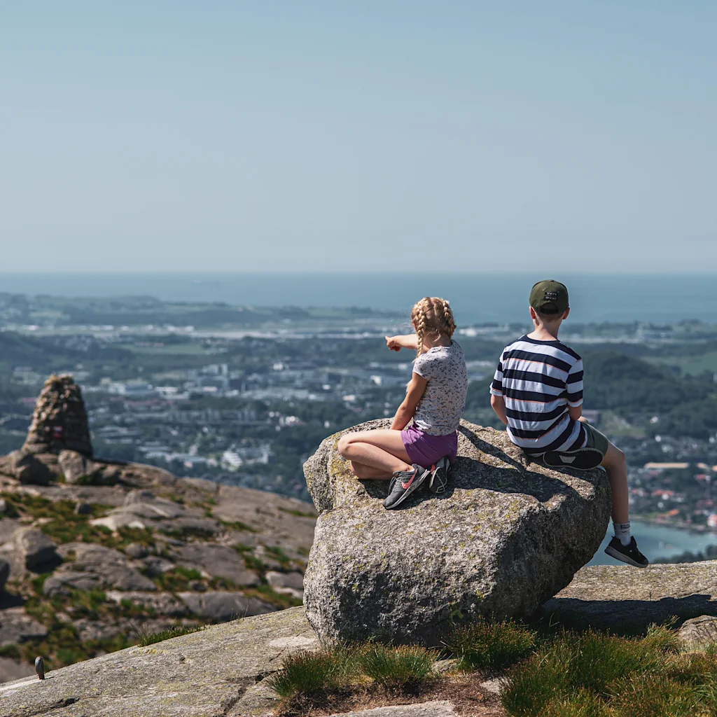 Kaksi lasta istuu vuorikivellä ja katselee panoraamanäkymää kaupunkiin ja mereen, toinen osoittaa etäisyyteen.