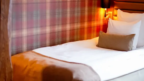 Et hyggeligt hotelværelse med en seng, ternet tapet og en varm lampe, der skaber en indbydende atmosfære.