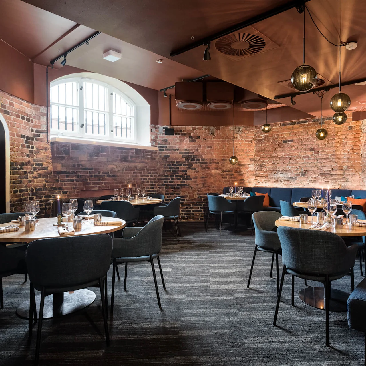 Elegantly set tables in a stylish restaurant with exposed brick walls and ambient lighting, creating a cozy dining atmosphere.