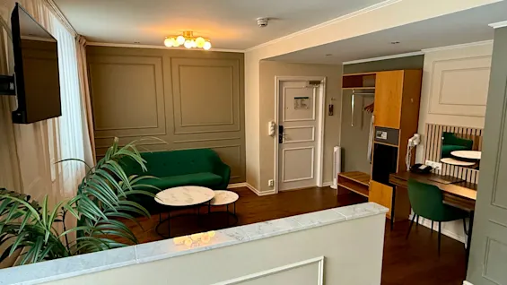 Tilava ja kutsuva hotellin juniorsviitti, jossa on vihreä sohva, työpöytä ja kasvi. Junior Suite, Comfort Hotel Linköping City.