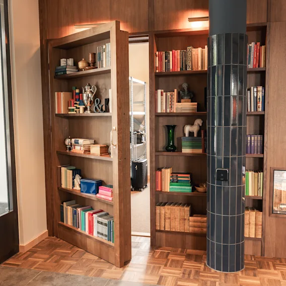 A cozy room with wooden bookshelves, one of which is a secret door slightly open, revealing another space.