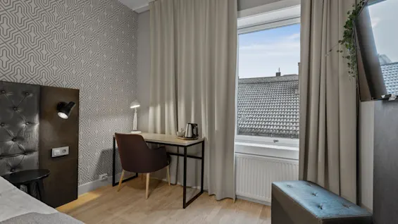 Ett mysigt hotellrum med en bekväm säng, en funktionell skrivbordsplats och ett fönster med utsikt över stadens takåsar.