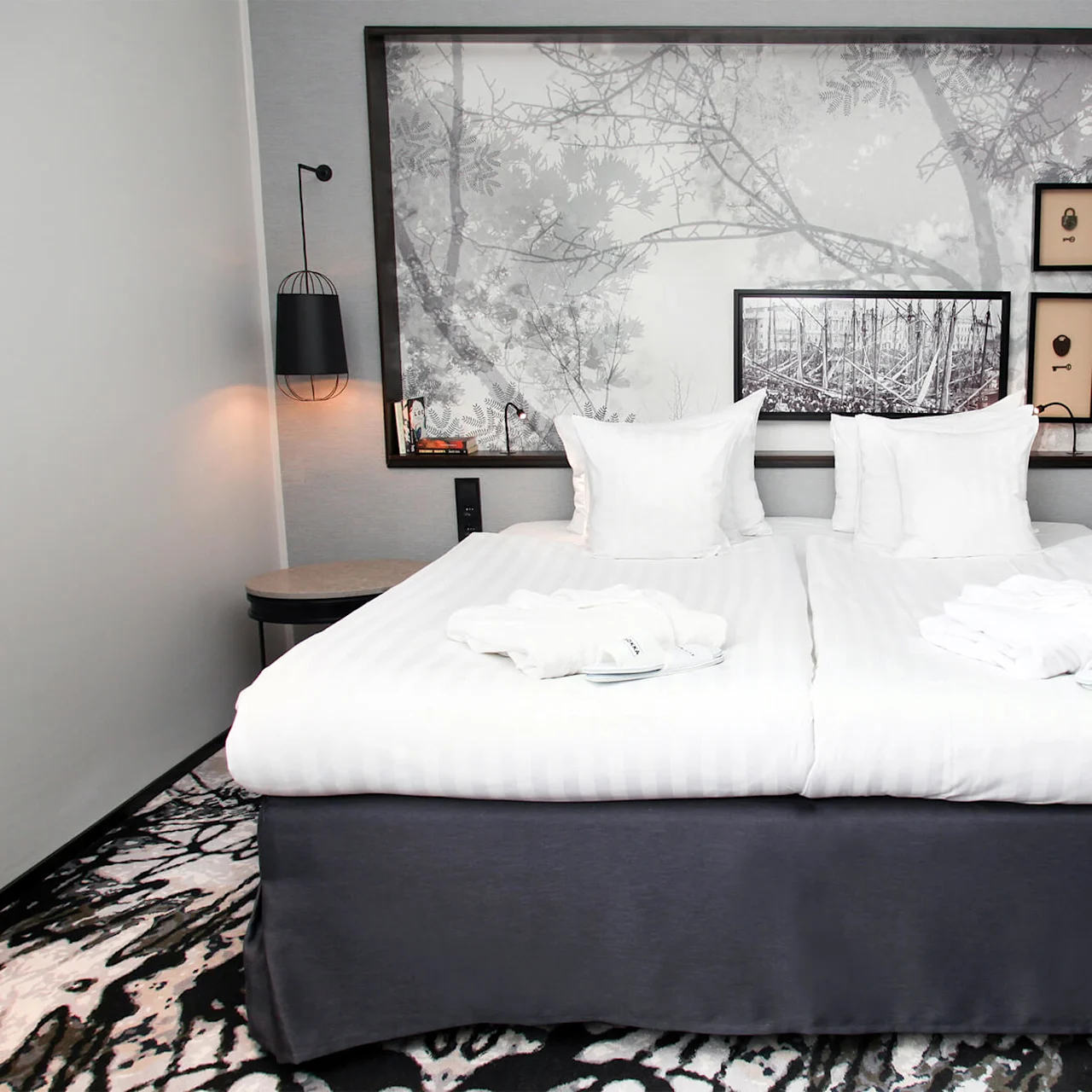 A neatly made double bed with white linens and pillows, positioned in a stylish hotel room with art on the walls.