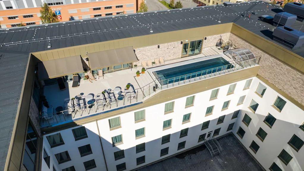 En takterrass har en rektangulär pool och sittplatser, omgiven av en modern byggnad. I närheten finns en skylt som säger "BALDER P" med annan otydlig skyltning på en angränsande vägg.
