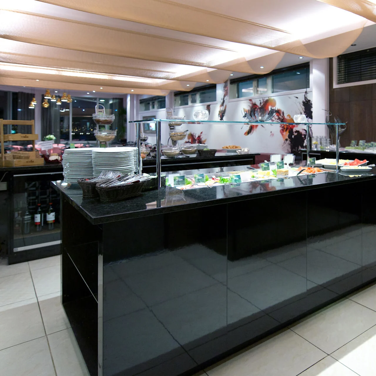 A buffet setup with plates, utensils, and a variety of foods in a modern dining area.