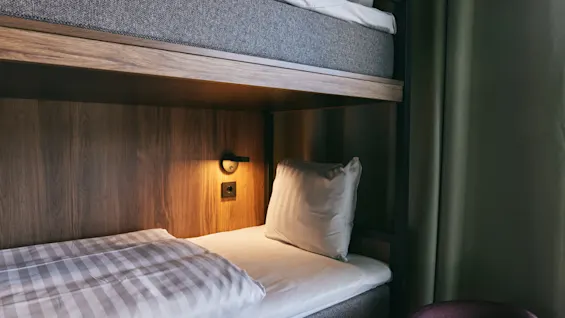 A cozy bunk bed in a room, with a warm light illuminating the wooden headboard and a made bed.