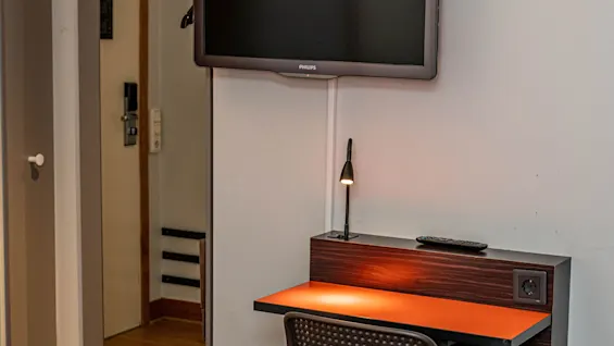 Ett hotellrum med en väggmonterad TV ovanför ett kompakt skrivbord och stol, vilket ger ett funktionellt utrymme för gäster.